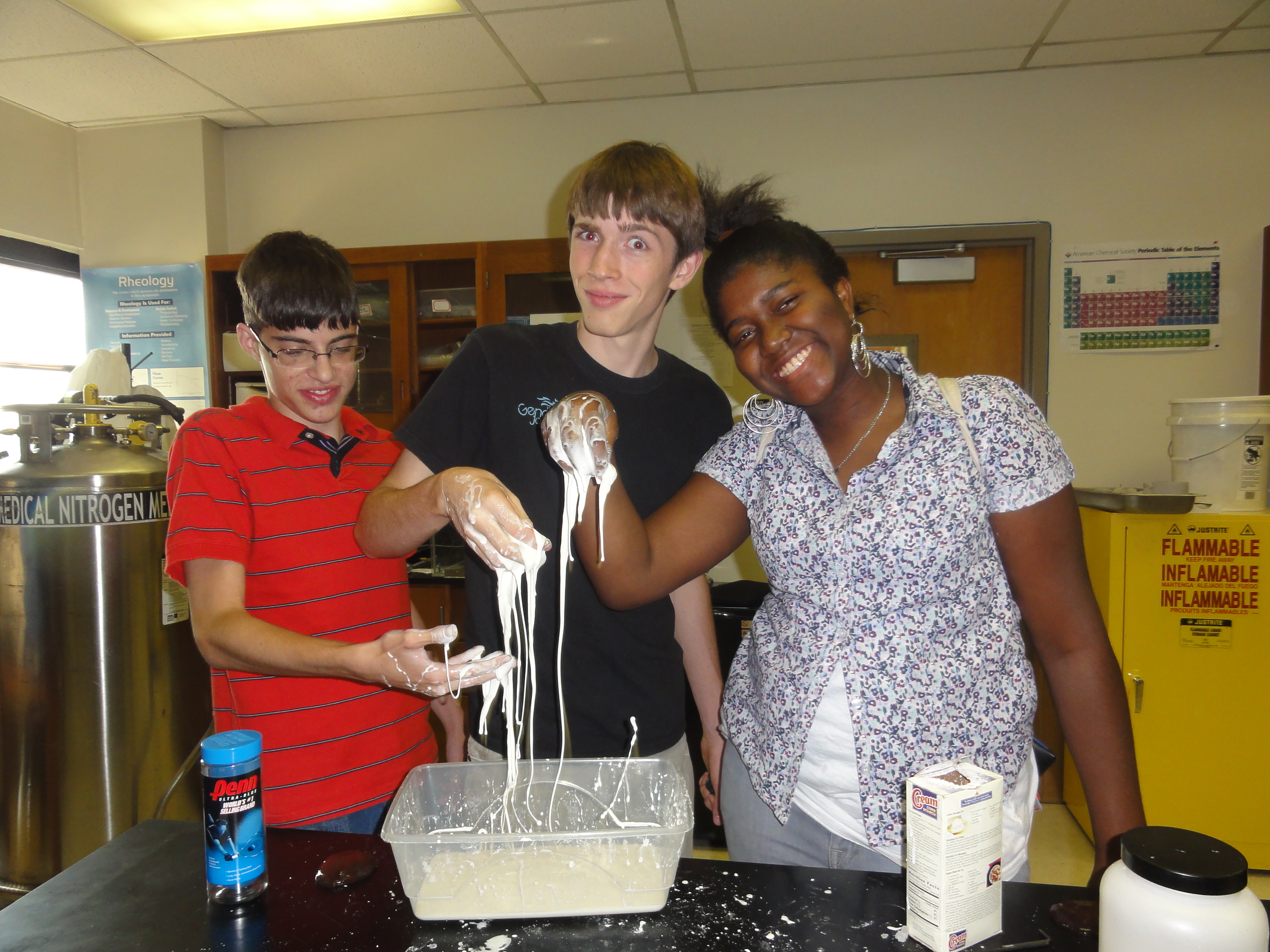 Three students each have a hand in a runny material with interesting properties.